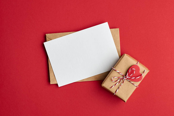 Valentines day card mockup with envelope and gift box with heart on red paper background, top view, copy space - Фото, зображення