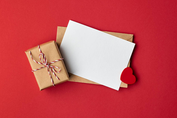 Valentines day card mockup with envelope and gift box with heart on red paper background - Valokuva, kuva