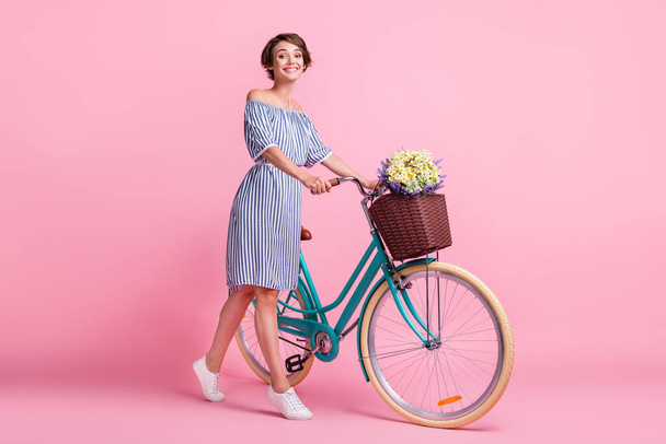 Photo portrait of cute woman holding bicycle with two hands isolated on pastel pink colored background - 写真・画像