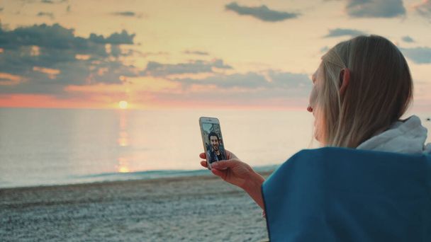 Νεαρή γυναίκα κάνει βιντεοκλήση στο φίλο της με smartphone στην παραλία - Φωτογραφία, εικόνα