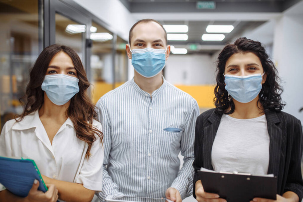 Tıbbi maske takan üç ofis çalışanının portresi iş ve gelecek beklentilerini tartışıyor. Yeni normal, sağlık hizmetleri, ofis hijyeni kavramı. Coronavirus karantina, salgın hastalık, yayılma önleme - Fotoğraf, Görsel