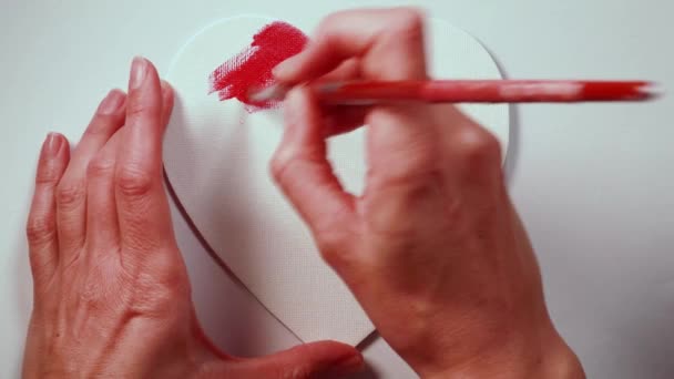 Vista superior de manos de mujer pintando un lienzo en forma de corazón rojo sobre fondo blanco. Timelapse vídeo con un concepto de amor. - Metraje, vídeo