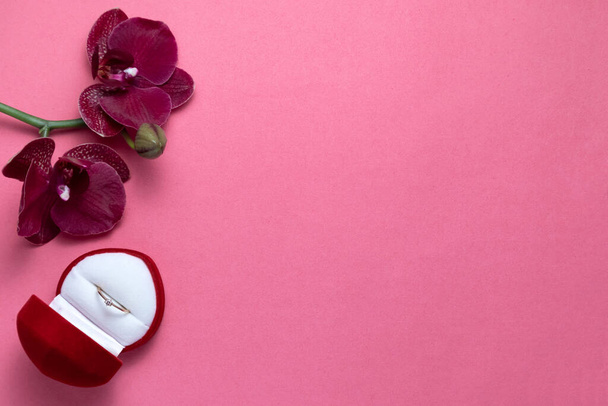 Wedding ring in a red box and red orchid on pink background. Valentines Day. - Photo, Image
