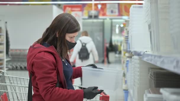 Chica en máscara y guantes compra contenedor de plástico de alimentos en la tienda - Metraje, vídeo