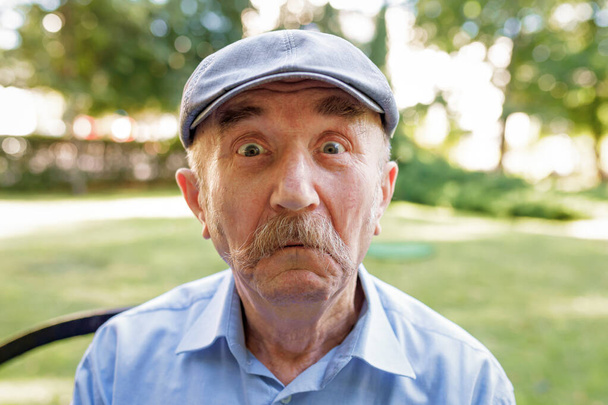 Portrét staršího muže s bílým knírkem, jak se dívá do kamery a dělá obličeje. Muž, který vypadá praštěně a legračně s pošetilým zkříženýma očima, vtipkuje a blbne. Detailní záběr, měkké zaměření - Fotografie, Obrázek