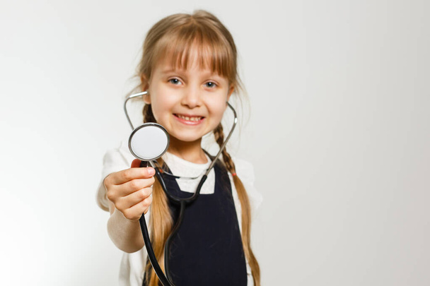 маленькая школьница изучает медицину с помощью фонендоскопа, изолированного по белому - Фото, изображение