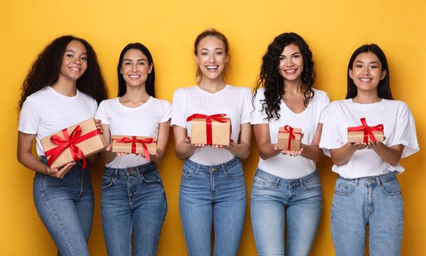 Счастливые разношерстные женщины держат подарочные коробки на желтом фоне - Фото, изображение