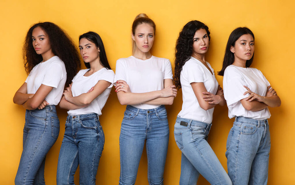 Unzufriedene Mixed Ladies posieren mit verschränkten Händen vor gelbem Hintergrund - Foto, Bild