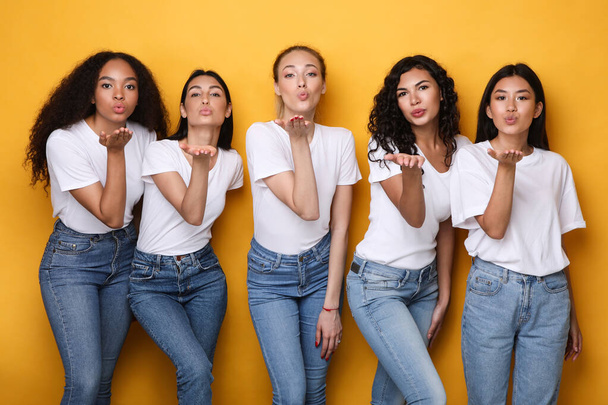 Cinque donne multiculturali felici che soffiano baci alla macchina fotografica, sfondo giallo - Foto, immagini