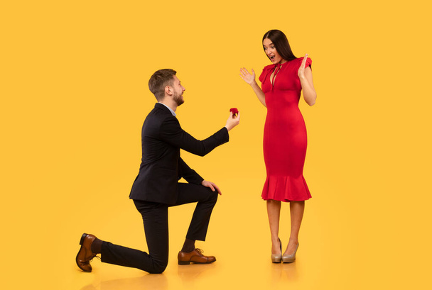 Man biedt meisje verlovingsring staande op knie, gele achtergrond - Foto, afbeelding