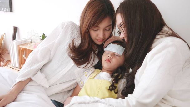 Szép család pár leszbikus anya vigyázni fogadott lánya beteg hűvös láz gél és kap jobb az ágyon otthon - Fotó, kép