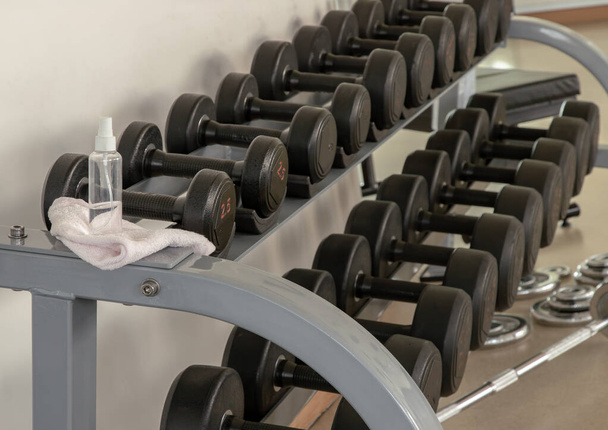 Cleaning exercise machines with alcohol sanitizer spray before lifting dumbbells in the gym or fitness. prevent Coronavirus infection,safety of the COVID-19 outbreak. Selective focus. - Foto, Imagem