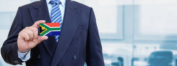 Imagen recortada del hombre de negocios con tarjeta de crédito de plástico con la bandera impresa de Sudáfrica. Fondo borroso. - Foto, Imagen