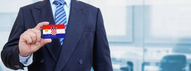 Cropped image of businessman holding plastic credit card with printed flag of Croatia. Background blurred. - Photo, Image