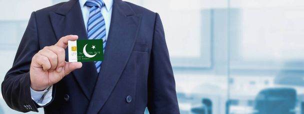 Pakistan 'ın baskılı bayrağıyla plastik kredi kartı tutan işadamının kesilmiş görüntüsü. Arkaplan bulanık. - Fotoğraf, Görsel