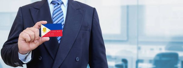 Cropped image of businessman holding plastic credit card with printed flag of Philippines. Background blurred. - Photo, Image