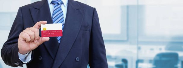 Imagen recortada del hombre de negocios sosteniendo una tarjeta de crédito de plástico con la bandera impresa de Polonia. Fondo borroso. - Foto, imagen