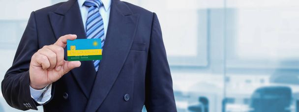 Cropped image of businessman holding plastic credit card with printed flag of Rwanda. Background blurred. - Photo, Image