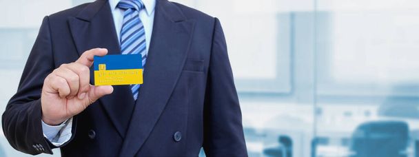 Gehakt beeld van zakenman met plastic creditcard met gedrukte vlag van Oekraïne. Achtergrond wazig. - Foto, afbeelding