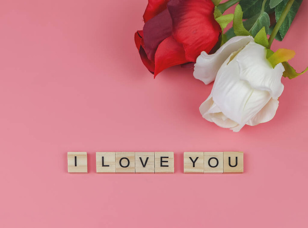 Bovenaanzicht of platte lay-out van houten letters Ik hou van je op roze achtergrond met rode en witte roos. Valentijnsdag en liefde concept. - Foto, afbeelding