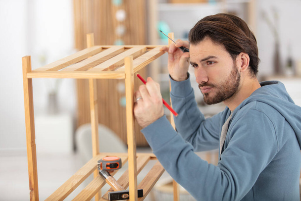 man installing wooden shelf at home - Фото, зображення