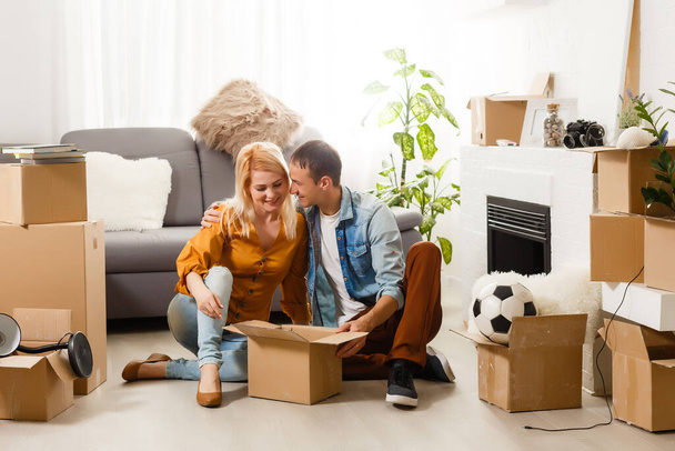 Όμορφο ζευγάρι κάθεται ανάμεσα σε πολλά κουτιά στο νέο τους σπίτι - Φωτογραφία, εικόνα