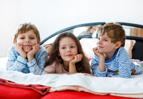 Drie gelukkige kinderen in pyjama 's die een pyjamafeest vieren. kleuterschool en school jongens en meisje hebben plezier samen - Foto, afbeelding