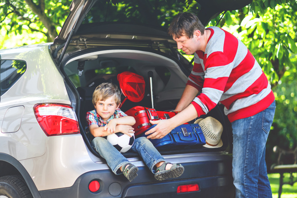 Little kid boy sitting in car trunk just before leaving for summer vacation. Dad packing suitcases. Happy family going on long journey during ockdown and quarantine time due corona pandemic disease - Foto, Imagen