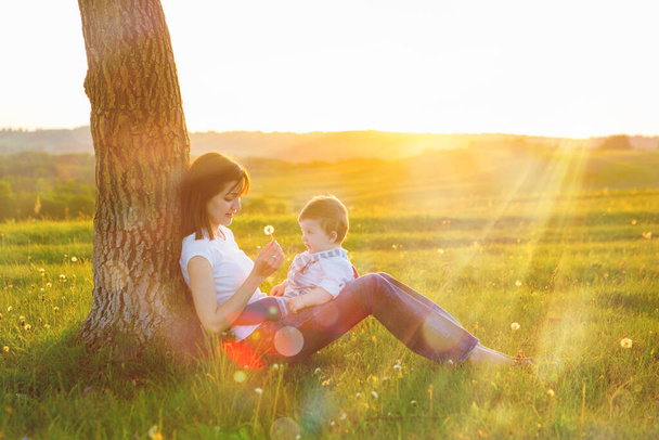 Portrait of picture of happy mother with baby on sunset background. Happy mother and son at sunset sunlight. - Foto, afbeelding