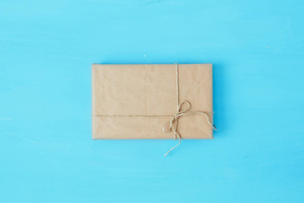 Overhead view of a single holiday package wrapped with eco friendly craft paper and tied with twine. Square format on a blue wooden table. - Фото, изображение