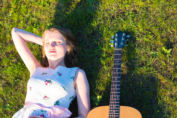 Beautiful hippie girl with guitar lying on the grass - Photo, image