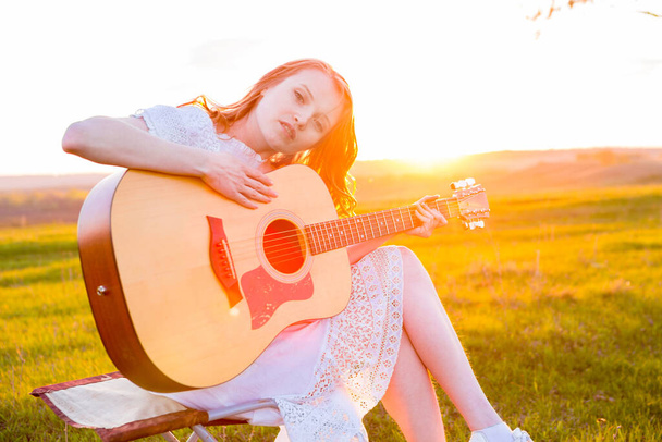 Beautiful young girl playing guitar in the field. Lens flare, selective focus, toned image. - Zdjęcie, obraz