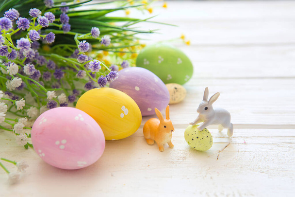 Easter eggs with flowers and rabbits toys on a white wooden table. - Foto, immagini