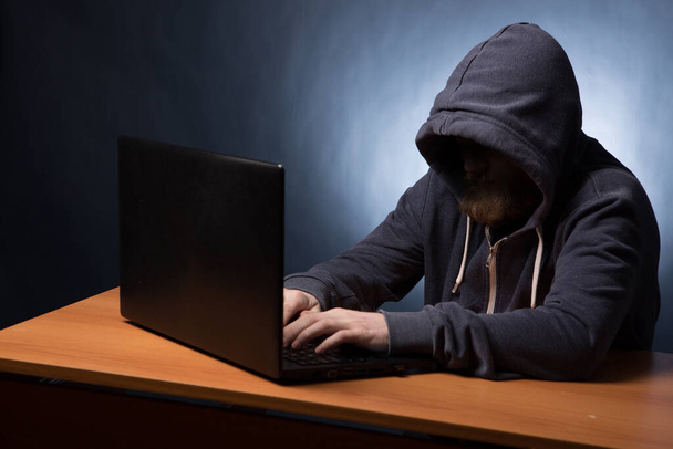Hooded computer hacker in hood stealing information with laptop - Fotoğraf, Görsel