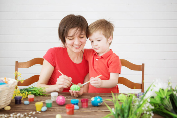 Smiling happy mother and child painting easter eggs. Happy family Mom and children son paint easter eggs with colors. Preparation for Easter holiday. - Zdjęcie, obraz