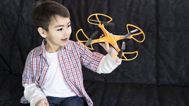 Egy kisgyerek otthon fog játszani egy quadcopterrel. A fiúnál van egy rádió vezérlő. otthoni életstílus. - Fotó, kép