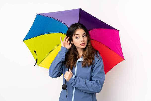 Woman holding an umbrella isolated on white background listening something - Photo, Image