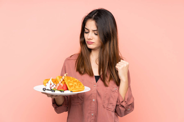 Young caucasian woman holding waffles isolated on pink background with sad expression - Photo, Image