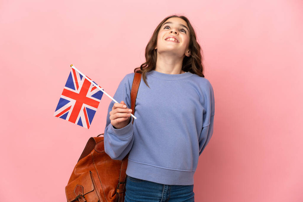 Kleines Mädchen mit einer Flagge des Vereinigten Königreichs auf rosa Hintergrund und Blick nach oben - Foto, Bild