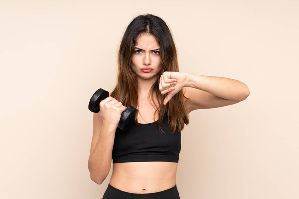 Young sport woman making weightlifting isolated on beige background showing thumb down sign - Foto, immagini