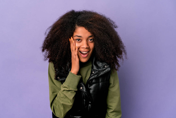 Young african american curly woman isolated on purple background shouts loud, keeps eyes opened and hands tense. - Photo, Image