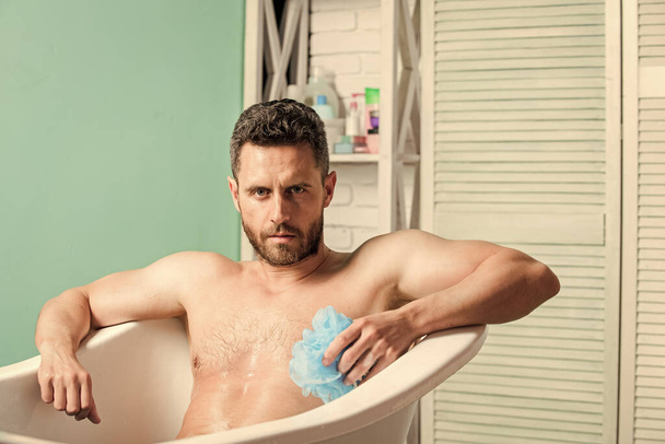 Men bodycare. Macho naked in bathtub. Sex and relaxation concept. man wash muscular body with foam sponge. macho enjoying bath. Sexy man in bathroom. Wash off foam with water carefully - Fotó, kép