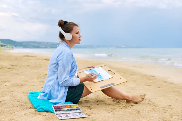 Relaxation on sea, mature woman in headphones with watercolors painting - Foto, Bild