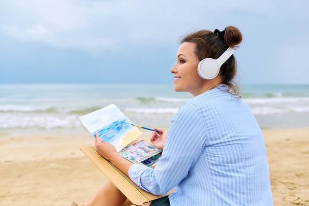 Relaxation on sea, mature woman in headphones with watercolors painting - Foto, Bild