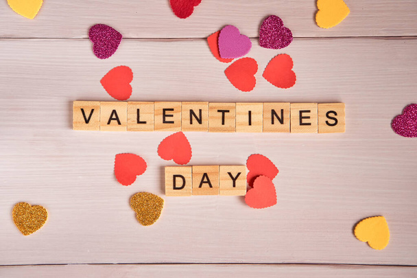Bovenaanzicht van het woord Valentijnsdag aangelegd uit vierkante houten tegels en rode, glanzend gele, paarse hartjes op oude witte houten achtergrond. - Foto, afbeelding