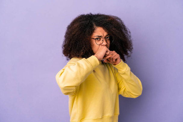 Jonge Afro-Amerikaanse krullende vrouw geïsoleerd op paarse achtergrond het gooien van een punch, woede, vechten als gevolg van een ruzie, boksen. - Foto, afbeelding