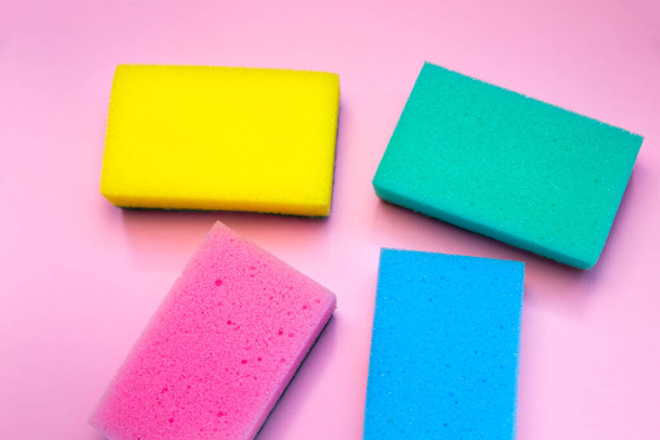 Esponjas coloridas para lavar los platos sobre fondo rosa. La fibra artificial no es una herramienta ecológica. Cosas para la cocina. - Foto, imagen