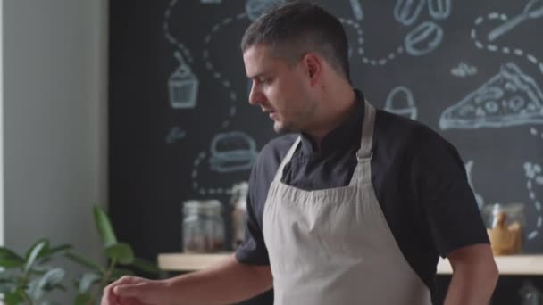 Handheld shot van mannelijke chef-kok in schort praten op camera, zet pan op fornuis en vervolgens gooien twee brood plakjes op het terwijl het geven van online kooklessen in de keuken - Video