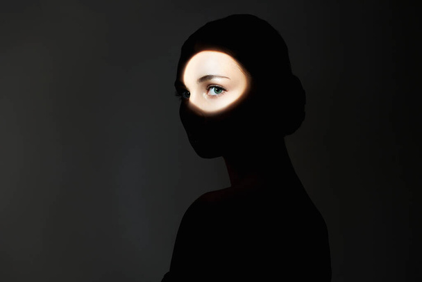 Silhouette eines schönen Mädchens in der Dunkelheit. junge Frau mit Schatten im Gesicht. weibliches Auge - Foto, Bild
