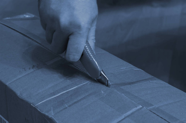 Image tonique déconcentrée d'une main découpant une boîte en carton avec un couteau. Processus de réception des achats en ligne. Concentration sélective. - Photo, image